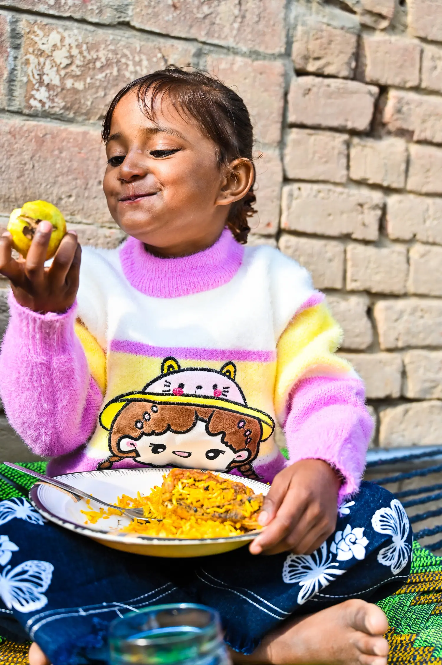 A small girl in new clothes eating apple and rice after being freed