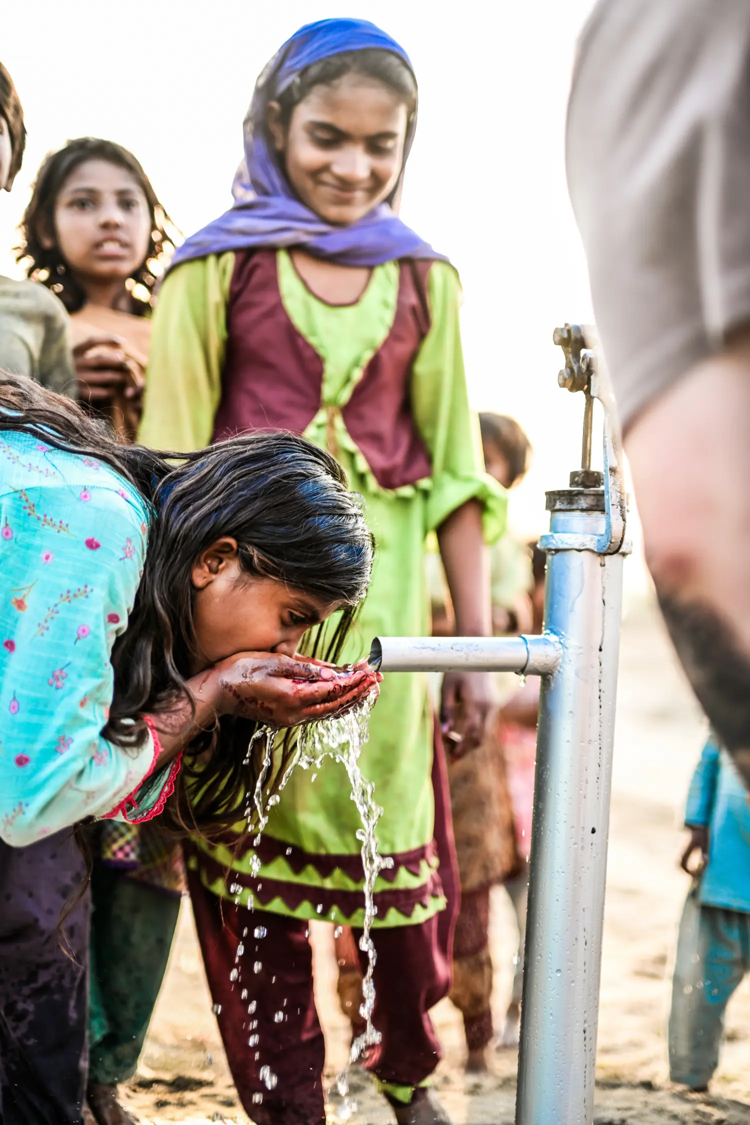 A young girl drinking clean water from a freshly installed hand pump for the first time
