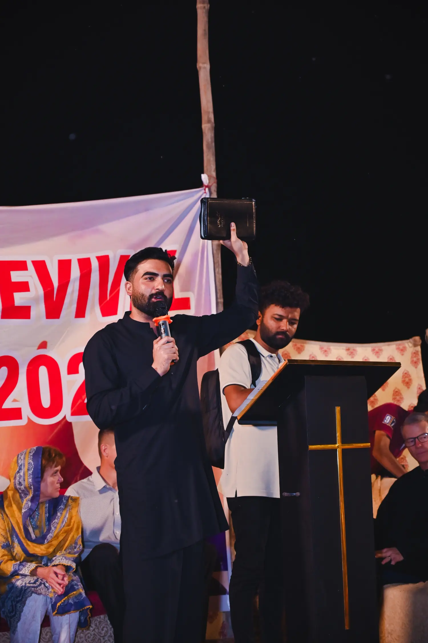 Pastor Ashkar Javed lifting up the Bible at a crusade